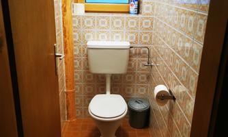 A simple bathroom with a toilet and a window. The walls are decorated with tiles and the floor is tiled.