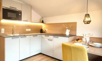 A modern kitchen with wood and white elements. A cozy table with yellow chairs invites you to eat.
