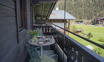 A cozy balcony with a table and two chairs, adorned with fresh flowers. In the background, green meadows and mountains can be seen.