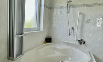 A modern bathroom with a spacious, white bathtub. There is a window that lets in light, and a shower bathtub with fixtures.