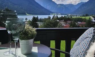 A beautiful view from a balcony of mountains and a lake. On the table are glasses and a plant.
