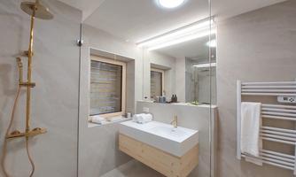 A modern bathroom with smooth, bright walls and an elegant shower. The vanity has a wooden surface and mirrors with LED lighting.