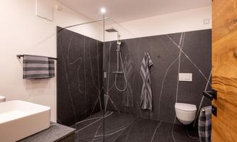 A modern bathroom with a rain shower and elegant stone surfaces. Towels and a towel holder complete the stylish design.