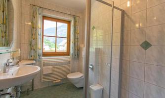 A modern bathroom with a shower, sink, and toilet. Large windows provide bright light and a pleasant view.