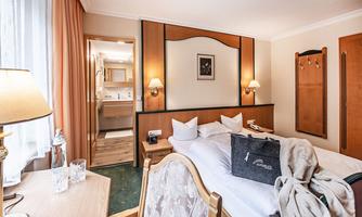 A cozy hotel room with two beds, a desk, and a wardrobe. The room is bright and friendly with warm colors.