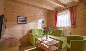 A cozy living space with wooden walls and a green sofa. Fresh roses are in a vase on the table.