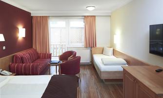 A cozy hotel room with a double bed, a sofa, and a color television. Large windows let in plenty of light.