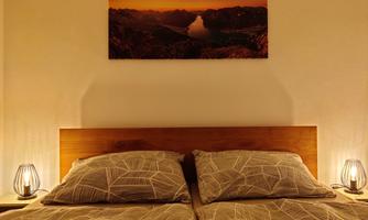 A cozy bedroom with a double bed and soft lighting. Above the bed hangs a picture of a landscape with a sunset.