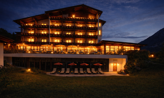 A beautiful hotel with illuminated balconies at dusk. In the foreground, sun loungers and umbrellas can be seen.