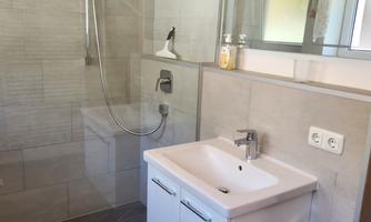 A modern bathroom with a glass shower cabin and an elegant sink. The space is designed to be bright and welcoming, with neutral colors and a small rug.