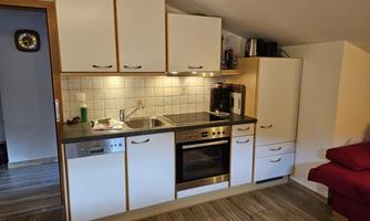 Small, modern kitchen with white cabinets and a cooking area. The countertop is made of wood and there is a red armchair in the background.