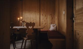 A cozy dining area made of wood with a table and heart-shaped chairs. Soft light from candles creates a warm atmosphere.