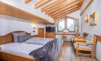 A cozy bedroom with a wooden beam ceiling and large windows. The room is equipped with a double bed, a television, and a seating area.