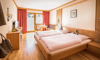 A bright room with wooden furniture and two single beds. The large windows let in plenty of daylight and provide access to a small balcony.