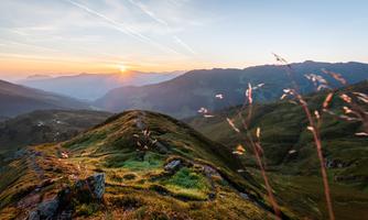 A picturesque mountain landscape at sunrise. Gentle hills and green meadows stretch to the horizon.