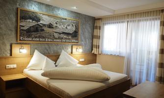 A cozy bedroom with a large bed and wooden details. The window lets in plenty of daylight.