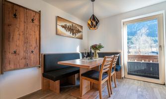 A cozy dining area with a wooden bench and a table. A beautiful view of the mountains is visible through the window.