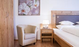 A cozy bedroom with a wooden bed and an armchair. A picture with flower motifs hangs on the wall.