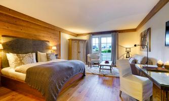 A stylish bedroom with wooden walls and a large bed. There is a cozy seating area and plenty of natural light from the windows.