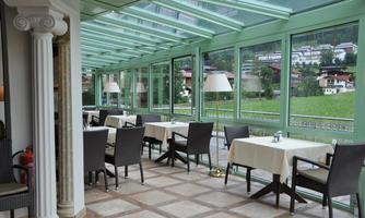 An elegant restaurant with large windows overlooking the green landscape. The tables are set and the space is friendly and inviting.