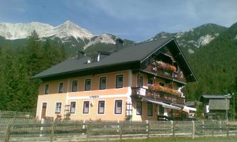 A charming alpine house surrounded by mountains and trees. The balconies are adorned with colorful flowers.