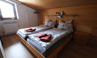 A cozy bedroom with two single beds and a wooden ceiling. The walls are made of wood and there are some decorative plants.