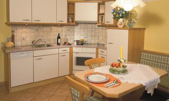 A modern kitchen with bright furniture and a cozy seating area. The table is beautifully set and there is fresh fruit on the table.