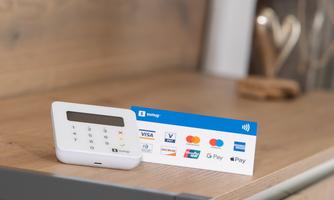 A modern payment device stands on a wooden surface. Next to the device lies a credit card with various payment methods.