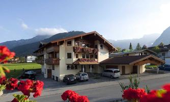 A charming house in the mountains with blooming window boxes. In the foreground, you can see flowers and a peaceful landscape.