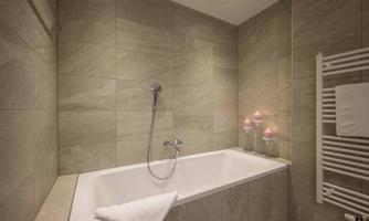 A modern bathroom with a bathtub and elegant stone walls. Soft lighting and candles create a relaxed atmosphere.