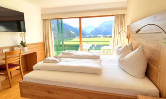 A modern room with a large bed and wooden interior. The view of the mountains and the landscape through the large windows creates a relaxing atmosphere.