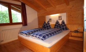A cozy bedroom with wood paneling and a large double bed. The bedding is checked and there is a window with a view of the greenery.