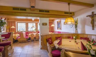 A cozy restaurant with wooden furniture and red accents. The tables are lovingly set, and there are large windows with a view outside.