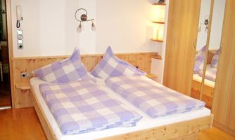 A cozy bedroom with a double bed and checkered blankets. The walls are light, and there is a large wardrobe.