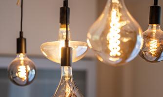 A creative light installation with various light bulbs hangs from a wooden branch. The combination of clear and matte colors creates a warm atmosphere.
