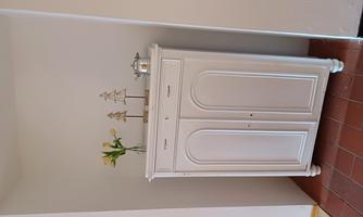 An elegant white cabinet stands against the wall. On it, there are a flower vase and decorative objects.