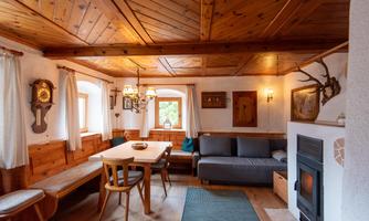 A cozy living room with wooden furniture and rustic charm. The room has large windows and a warm atmosphere.