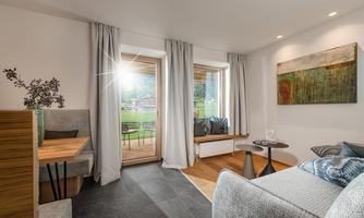 A modern living and dining room with large windows and a view of the outdoors. The furniture is stylish and the decor feels bright and inviting.
