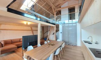 A modern living room with an open kitchen and a large dining table. The decoration is simple and elegant, with plenty of natural light.