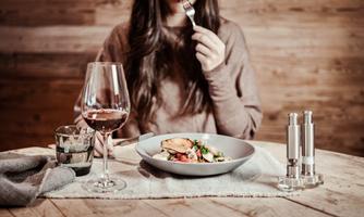 A woman is sitting at the table and enjoying a meal. On the table, there are a wine glass and a water glass, as well as spice mills.