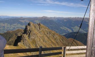An impressive mountain peak with a wide view of the surrounding valleys. The sky is clear and the landscape is characterized by gentle hills and mountains.