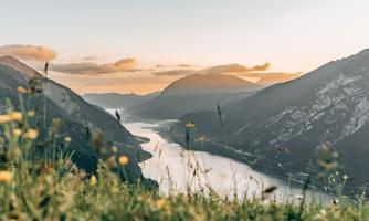 A picturesque landscape with mountains and a river that gently flows between them. The sunset colors the sky in warm tones.