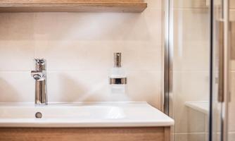 A modern bathroom with an elegant sink and a stainless steel faucet. The walls are light, and the furniture is made of wood, creating a friendly atmosphere.