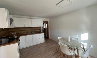 A modern kitchen with white furniture and wooden details. Stylish white chairs are at the table.