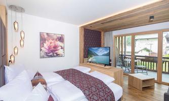 A modern hotel room with a large bed and elegant furnishings. A TV and a balcony with a view are also available.