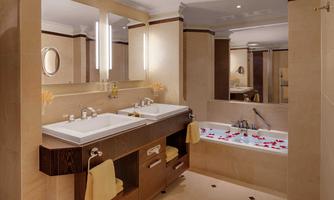 An elegant bathroom with two sinks and a large bathtub. The tub is decorated with rose petals, and the walls are painted in warm tones.