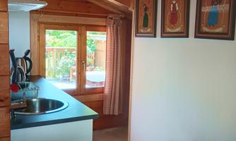 A small kitchen with a wash basin, electric stovetop, coffee maker, water boiler. At the end of the room there is a window with a view to the patio.