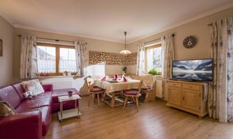 A cozy living room with a red sofa and a dining table. A television and large windows create a bright atmosphere.