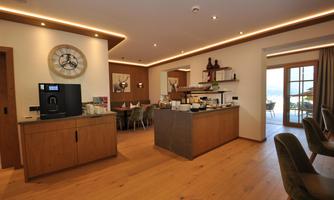 A modernly designed room with a coffee bar and wooden shelves. Large windows provide a view outside and ensure bright light.