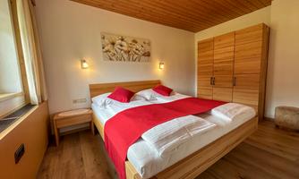 A cozy bedroom with a double bed and red bedding. The room has wooden paneling and a beautiful view through the window.